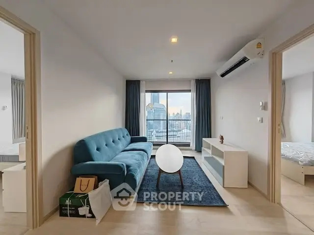 Modern living room with blue sofa and city view from balcony in high-rise apartment.