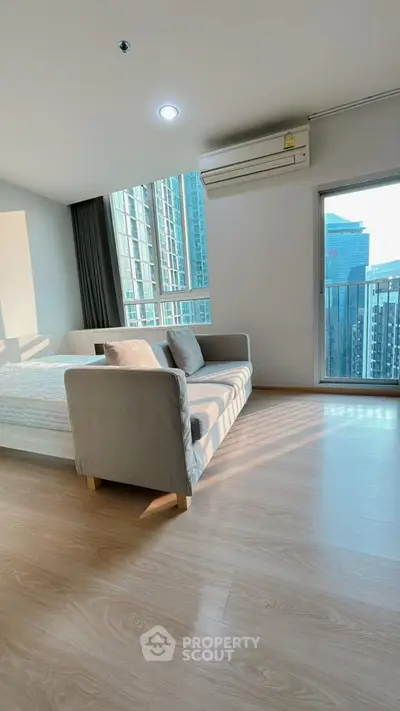 Modern living room with city view and natural light, featuring sleek sofa and wooden flooring.