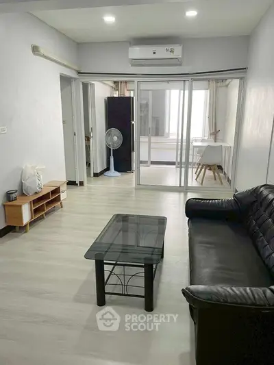 Spacious living room with modern furnishings and glass partition leading to a bright study area.