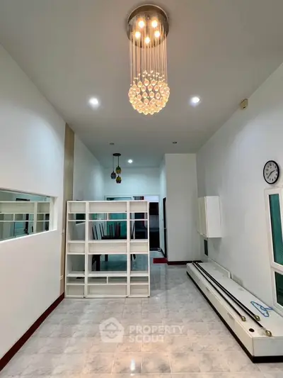 Spacious modern living room with elegant chandelier and sleek shelving unit.