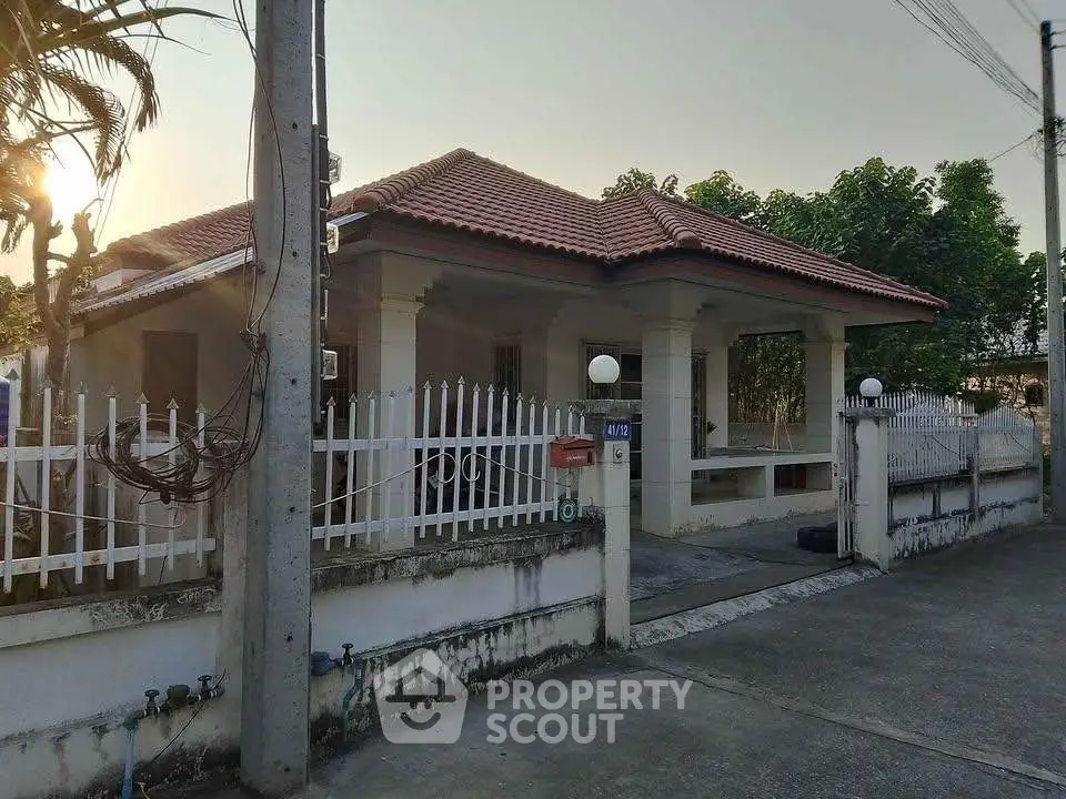Charming single-story house with red tile roof and white fence in a serene neighborhood.