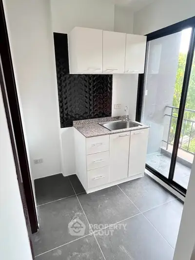 Modern compact kitchen with sleek cabinets and balcony access in a stylish apartment.