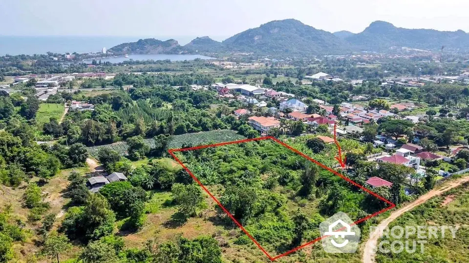 Expansive lush green land parcel available, outlined for clarity, with scenic mountain views and nearby community, ideal for development.