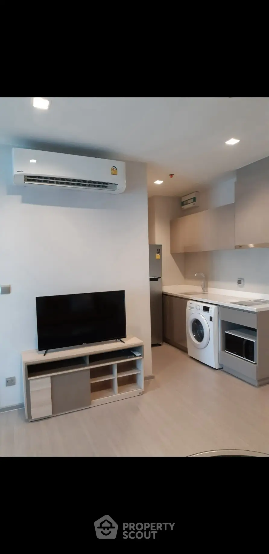 Modern compact living room with integrated kitchen featuring appliances and sleek design.