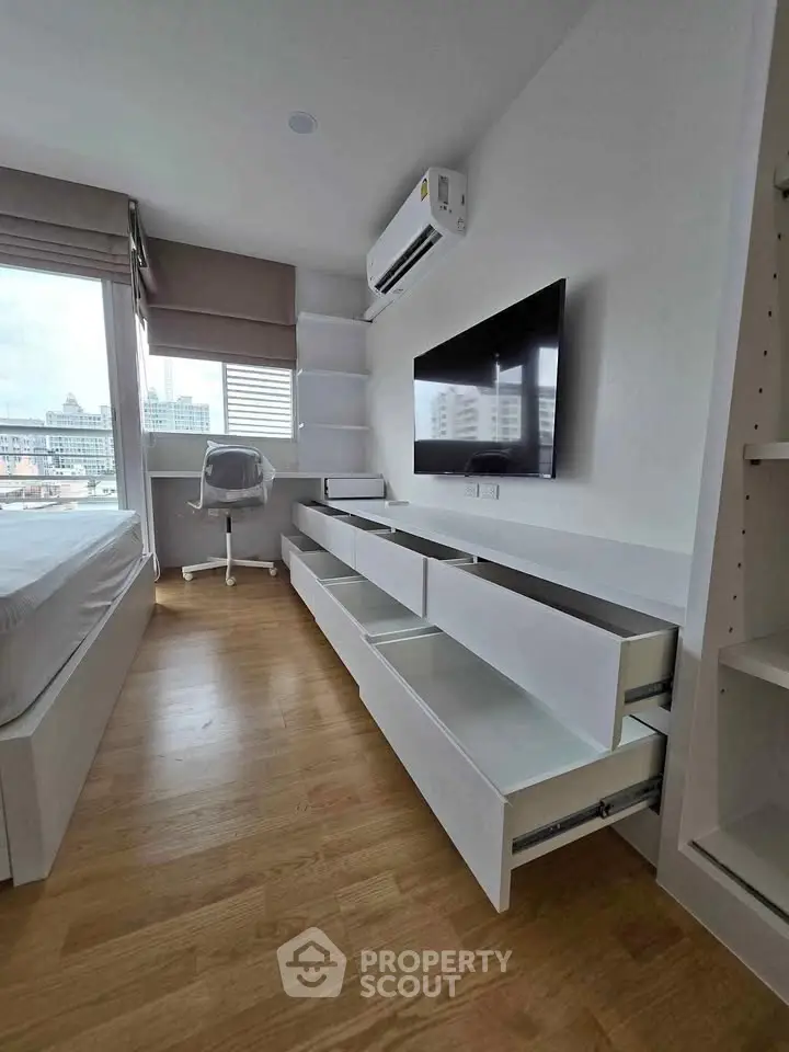Modern bedroom with sleek storage and city view, featuring hardwood floors and wall-mounted TV.