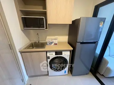 Modern kitchen with washing machine, microwave, and fridge in compact layout.