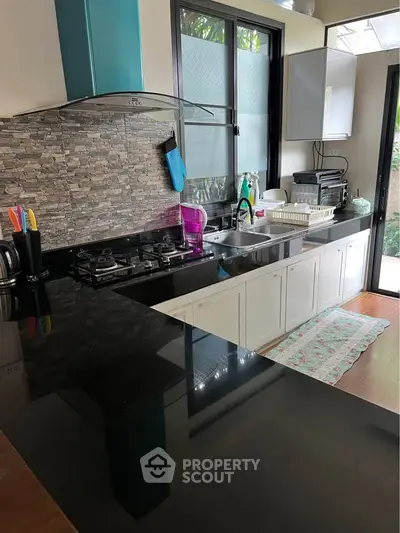 Modern kitchen with sleek black countertops and gas stove, featuring a stylish backsplash and ample natural light.