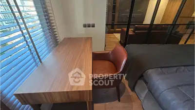 Modern bedroom with study area featuring a sleek wooden desk and leather chair, offering city views through large windows.