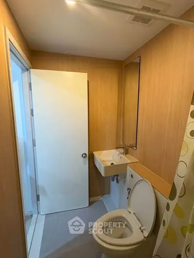Compact bathroom with modern fixtures and wooden paneling, featuring a toilet and sink.