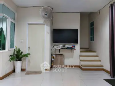 Modern living room with wall-mounted TV, staircase, and indoor plant for a cozy ambiance.