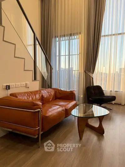 Elegant living room with high ceilings and modern furniture, featuring a leather sofa and stylish glass coffee table.