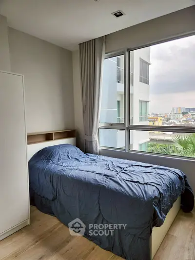 Cozy bedroom with large window offering city views and natural light.