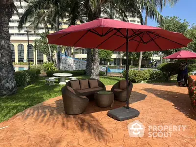 Luxurious outdoor seating area with umbrella by the poolside in a tropical garden setting.