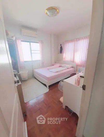 Cozy bedroom with pink accents and natural light, featuring a comfortable bed and air conditioning.