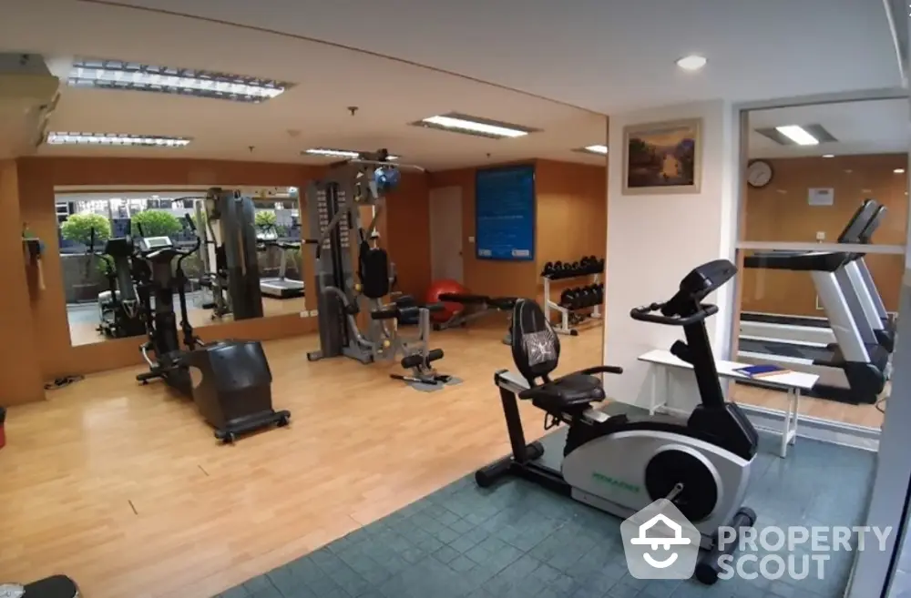 Spacious and well-equipped residential gym with modern fitness machines, mirrored walls, and ample lighting, perfect for a healthy lifestyle.