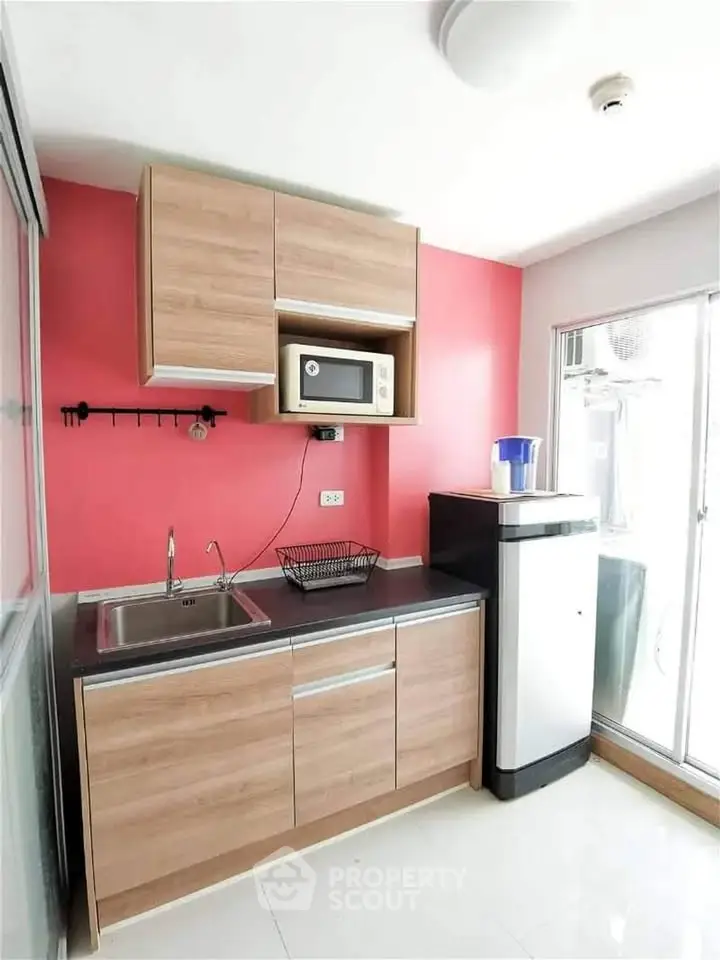 Modern kitchen with wooden cabinets, microwave, and compact fridge in bright space.