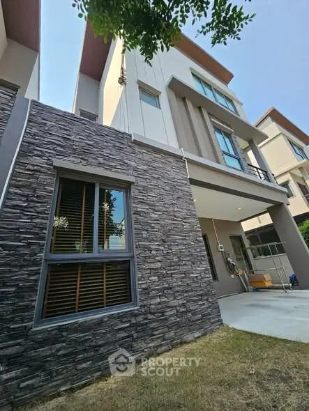 Modern multi-story house with stone facade and lush green lawn