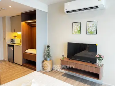 Modern studio apartment with sleek design, featuring a cozy bed, wall-mounted TV, and compact kitchenette.
