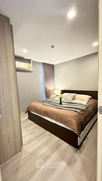 Modern bedroom with cozy decor and natural light, featuring sleek wooden flooring and neutral tones.