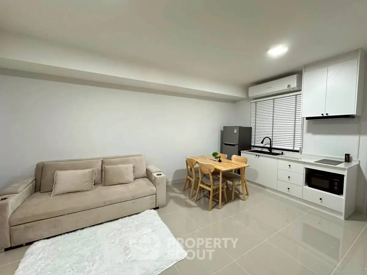 Modern open-layout living room with cozy sofa, dining set, and sleek kitchen appliances.