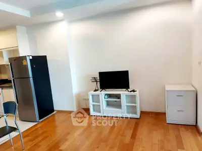 Modern living room with wooden flooring, sleek furniture, and a stainless steel fridge in an open layout.