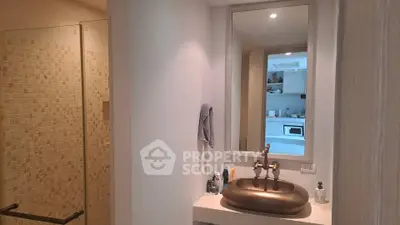 Modern bathroom with stylish sink and large mirror reflecting kitchen view.
