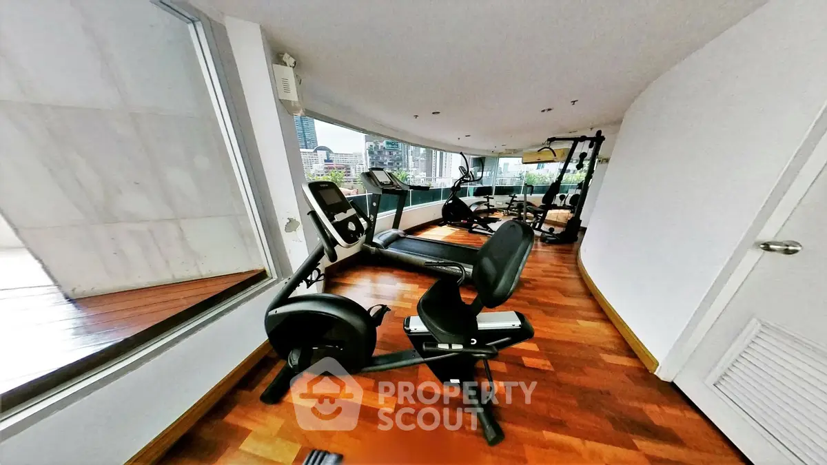 Spacious gym with modern equipment and city view in luxury apartment building.