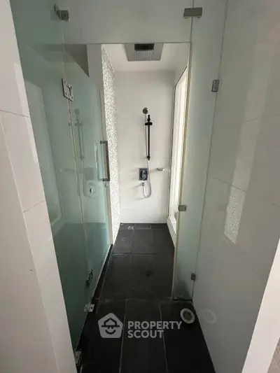 Modern minimalist bathroom with glass shower enclosure and sleek black tiles.