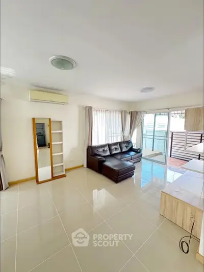 Spacious living room with modern sofa and large windows leading to balcony.