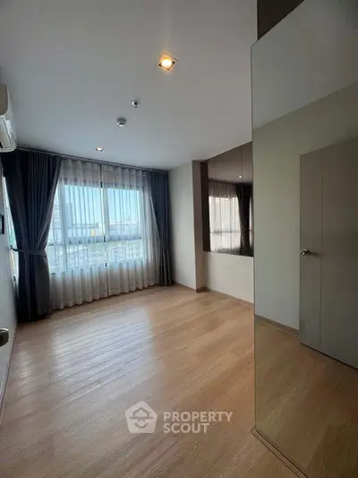 Spacious empty bedroom with large window and wooden flooring in modern apartment.