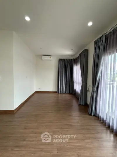 Spacious empty room with wooden flooring and large windows with curtains, ideal for customization.