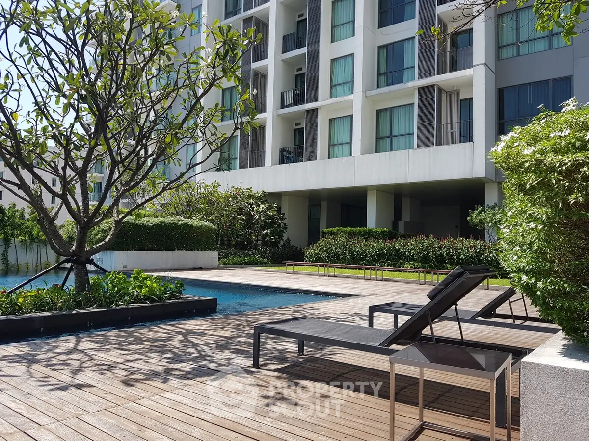Luxurious apartment complex with poolside relaxation area and lush greenery.