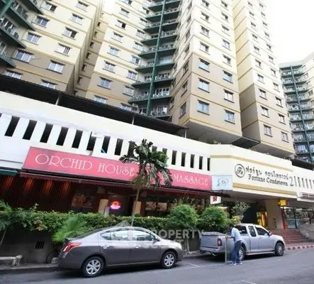 High-rise condominium building with street-level shops and parked cars.