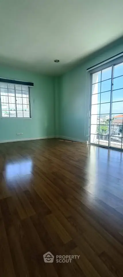 Spacious empty room with wooden flooring and large windows offering city views.