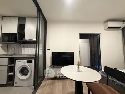 Modern studio apartment with open layout, featuring a compact kitchen and living area with washing machine and TV.