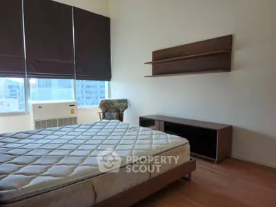 Spacious bedroom with large window and modern furniture in a high-rise apartment.