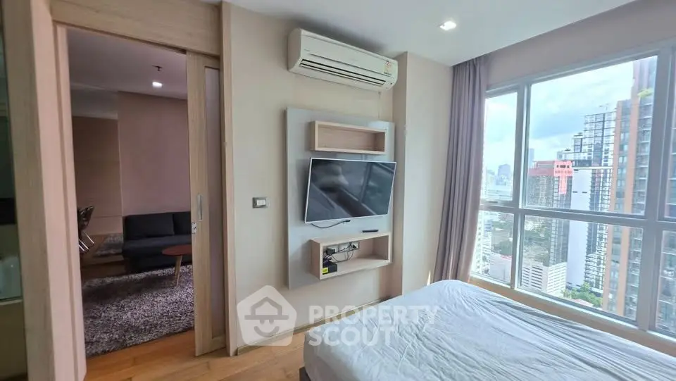 Modern bedroom with city view, featuring a wall-mounted TV and air conditioning, adjacent to a cozy living room.