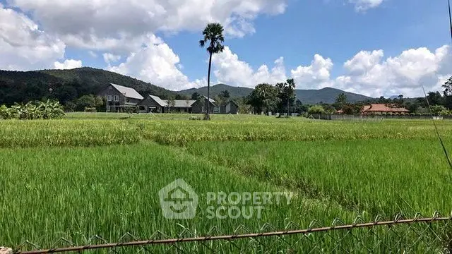 Scenic view of lush green fields with distant houses and mountains under a blue sky.