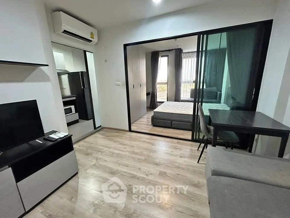 Modern apartment interior with open layout, featuring a cozy living area and bedroom separated by glass doors.