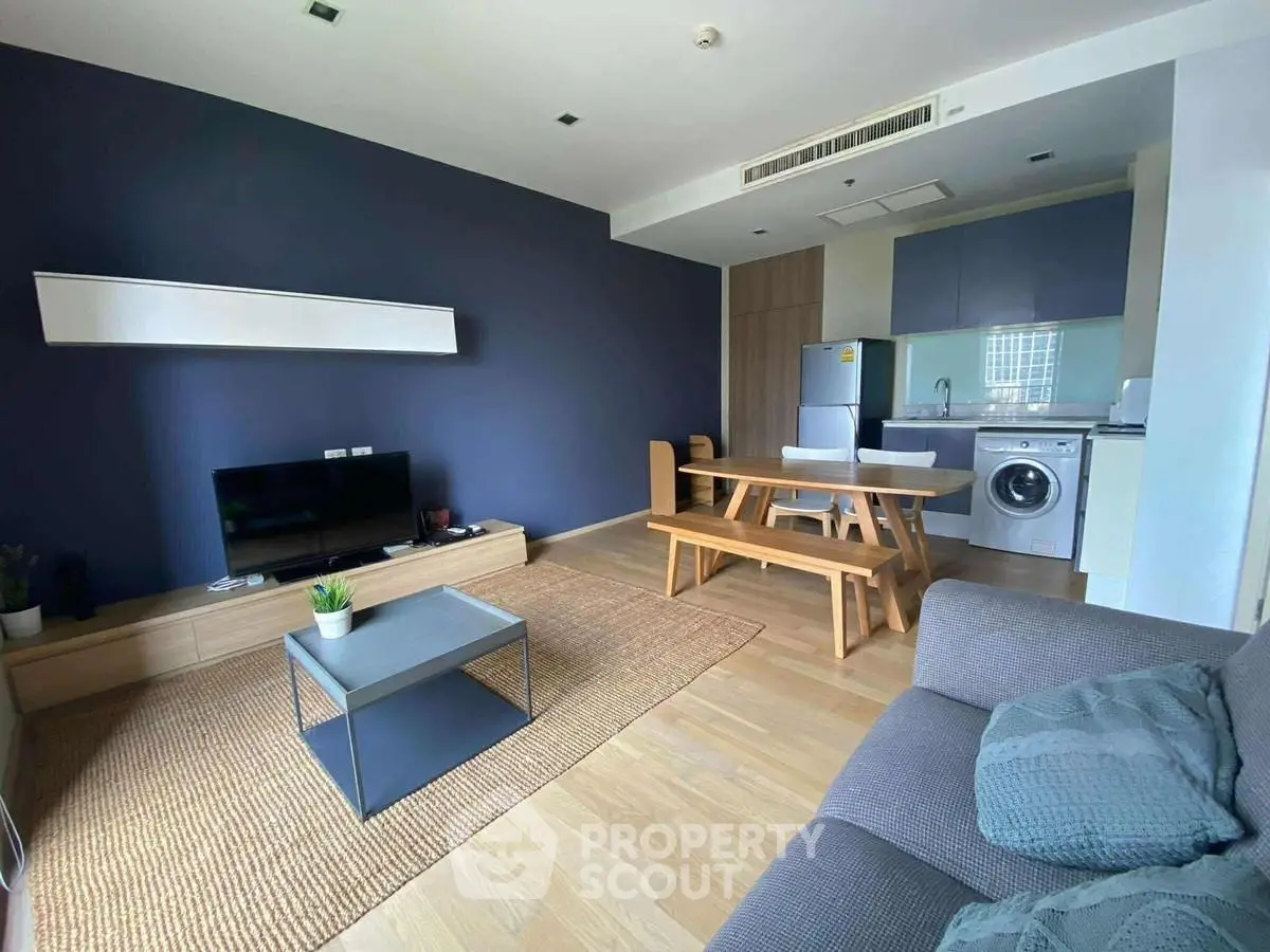 Modern living room with stylish furniture and open kitchen layout, featuring a washing machine and dining area.