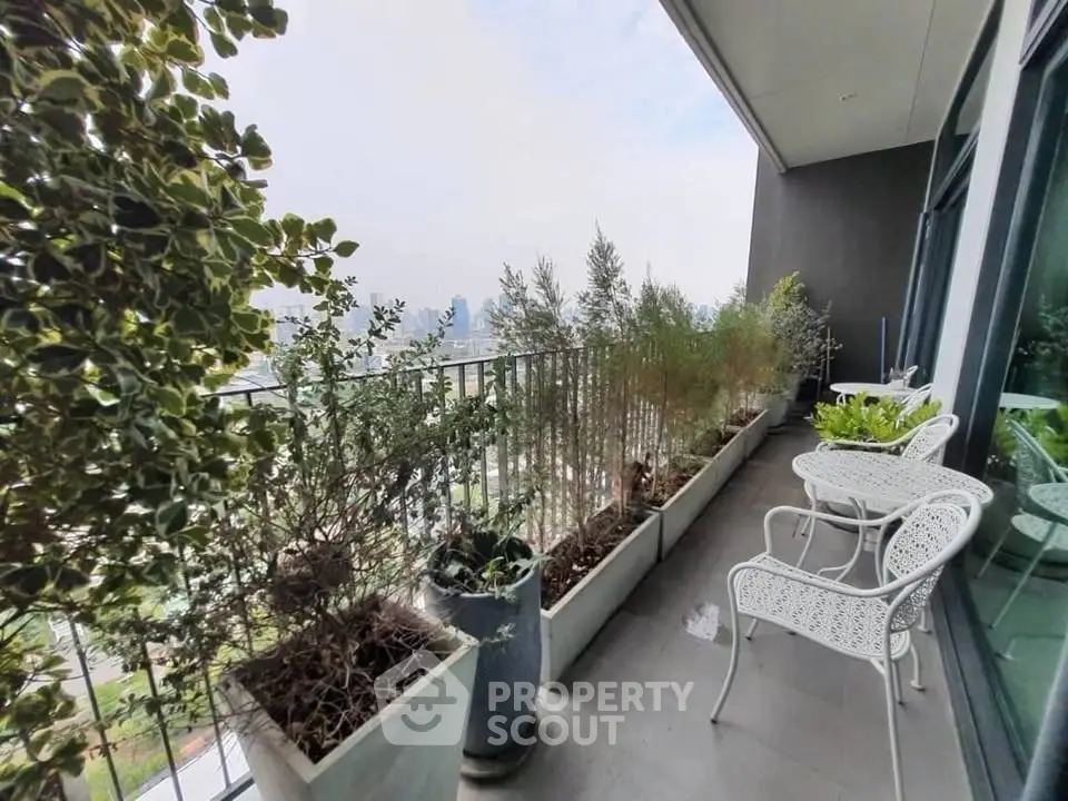 Spacious balcony with city view, featuring elegant white furniture and lush greenery, perfect for relaxation.
