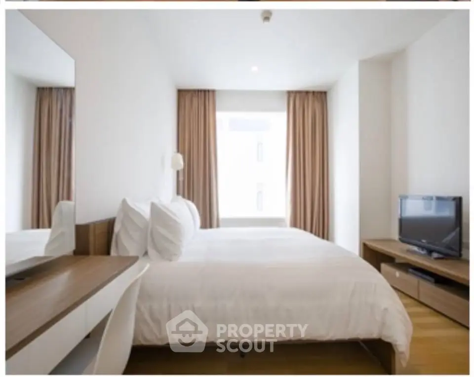 Modern bedroom with cozy bed, wooden furniture, and natural light from large window.