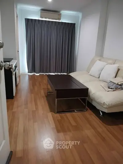 Cozy living room with wooden flooring, modern sofa, and air conditioning, perfect for relaxation.