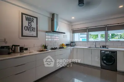 Modern kitchen with sleek white cabinets, gas stove, and washing machine, offering a stylish and functional space.