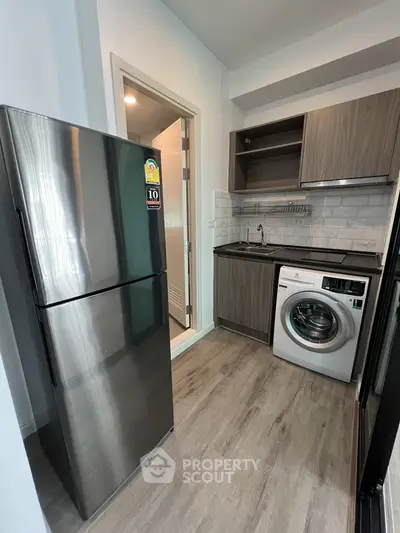 Modern kitchen with stainless steel fridge and washing machine in compact layout.