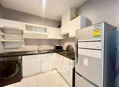 Modern kitchen with sleek white cabinets, stainless steel fridge, and washing machine in a compact layout.