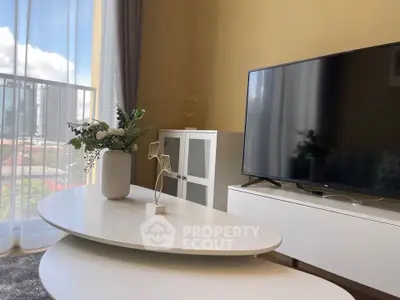 Modern living room with stylish furniture and large TV, featuring a bright window view.