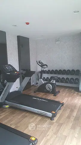 Modern gym with treadmill, exercise bike, and dumbbells on wooden flooring.