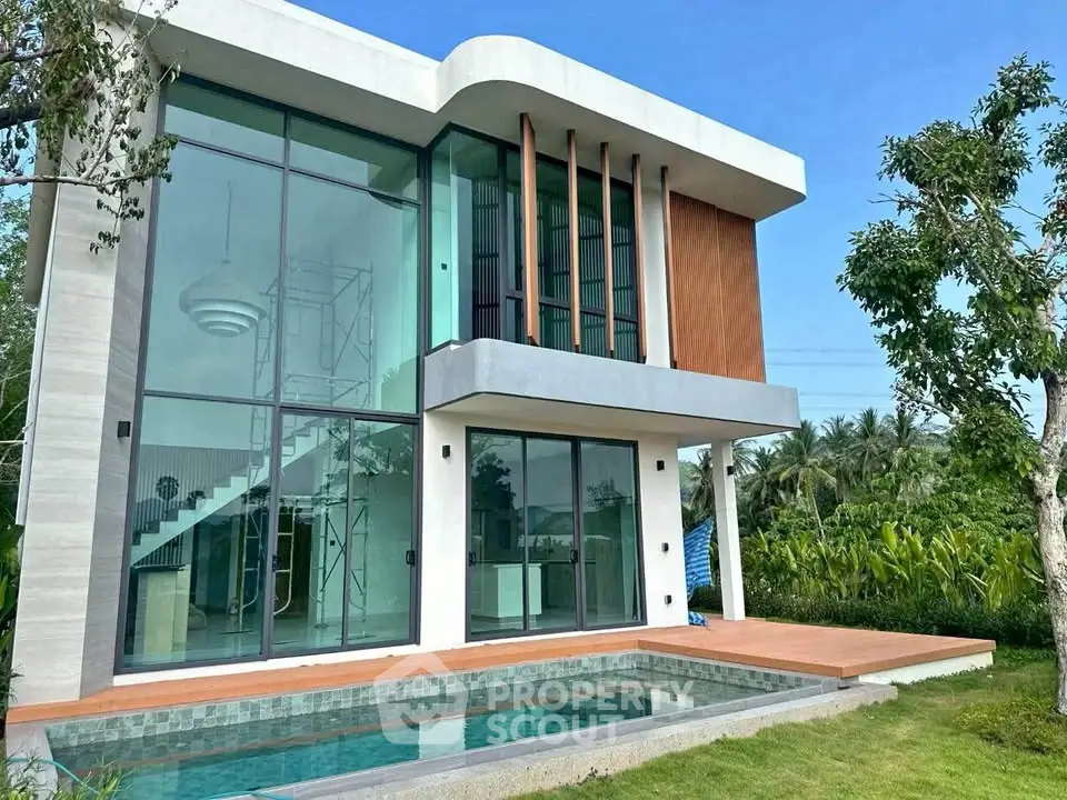 Modern two-story house with large glass windows and private pool in lush green setting.