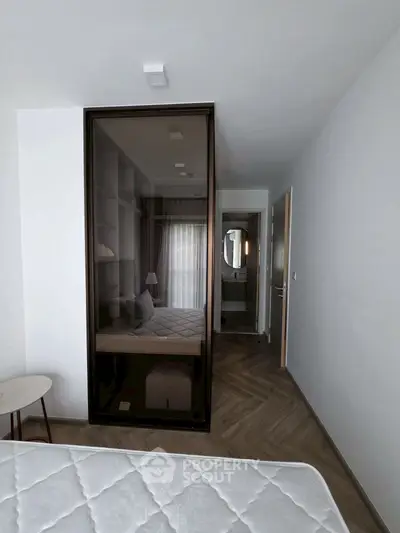 Modern bedroom with glass wardrobe and herringbone flooring, leading to a stylish bathroom.